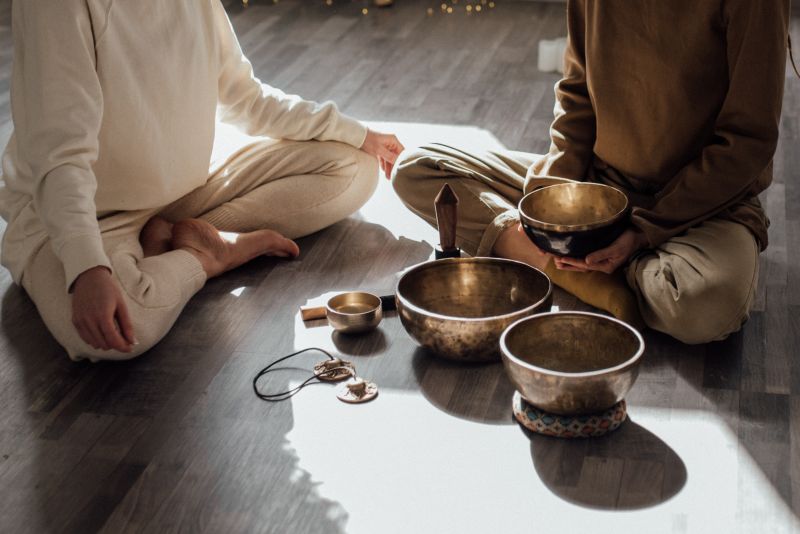 Two people sitting cross-legged holding small brass bowls.
