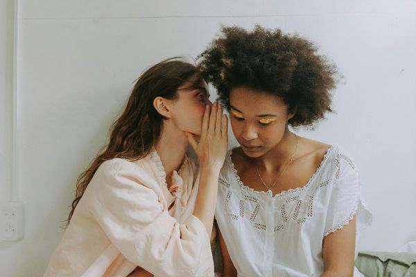 A woman whispers into the ear of another.