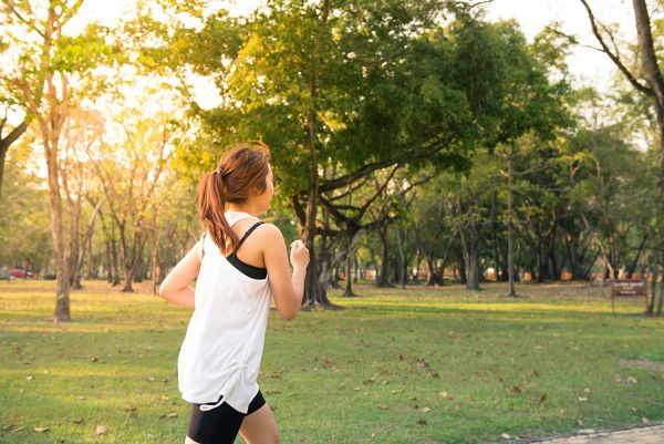 A woman runs in a park with early morning sunlight.
